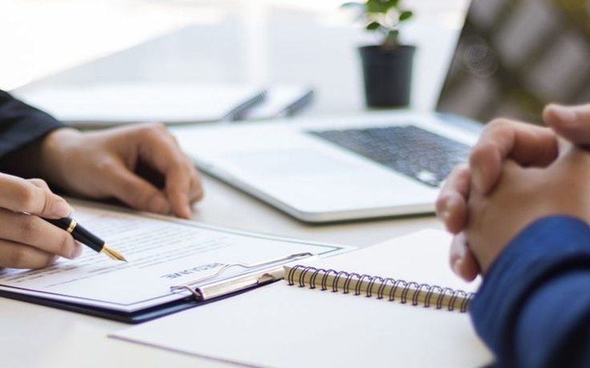 Profissionais analisam documentos e conversam à mesa em ambiente de trabalho.